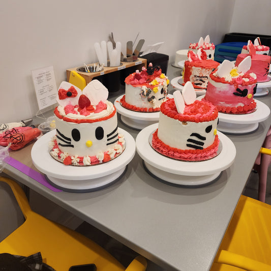 A table filled with custom Hello Kitty cakes decorated during a DIY cake-decorating party, each unique.