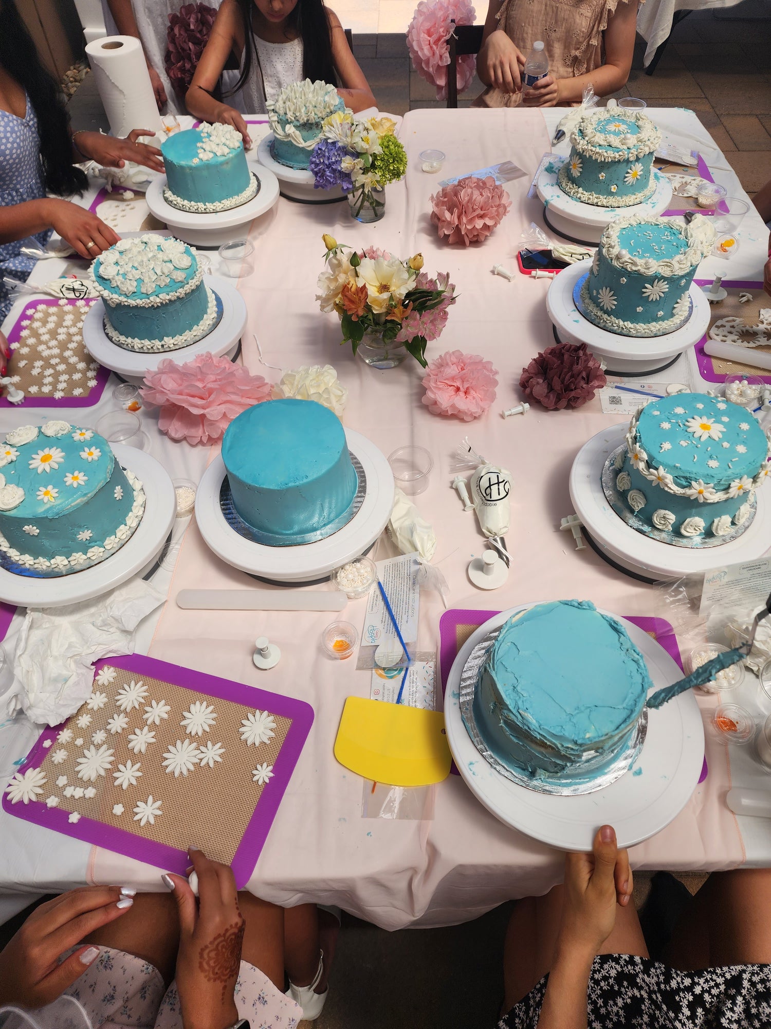 Teenage girls decorate blue cakes with white frosting and daisies at a to-go DIY cake-decorating party supplied by Cake Hoopla