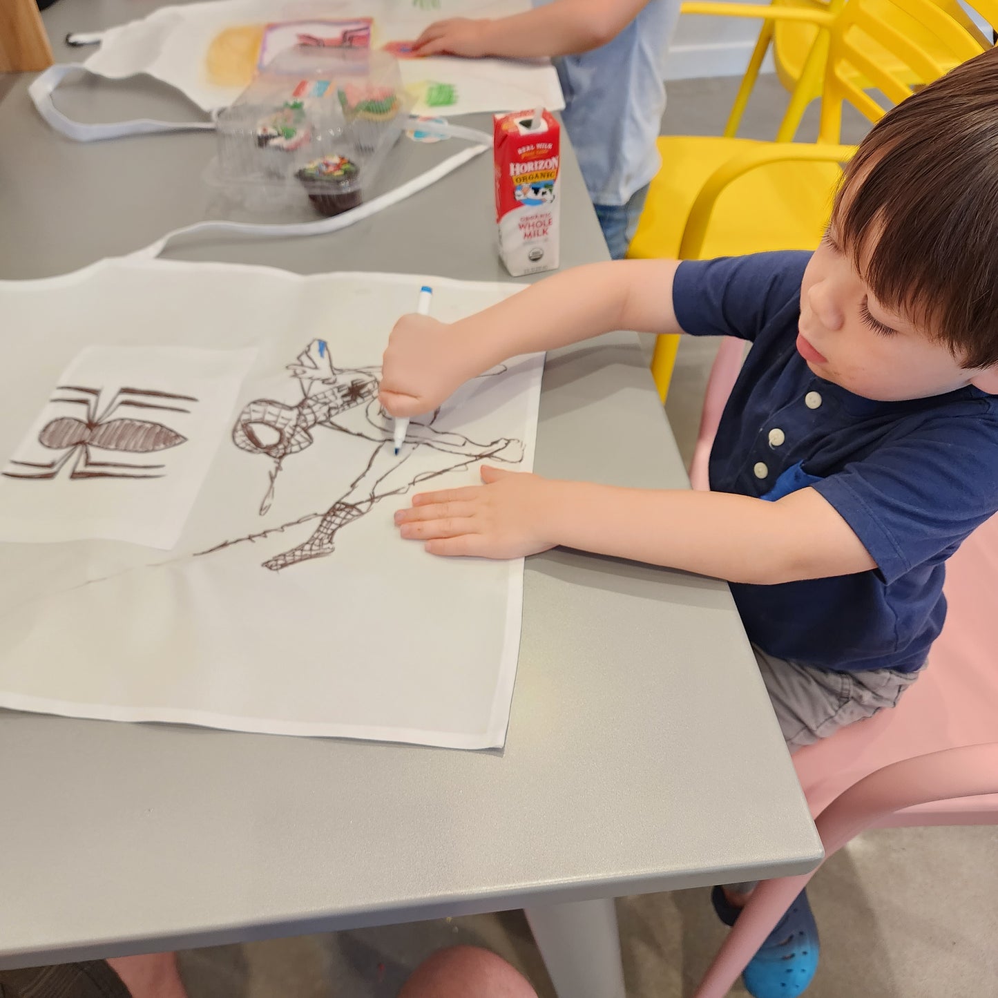 a young boy colors an apron with fabric markers during an in-studio party