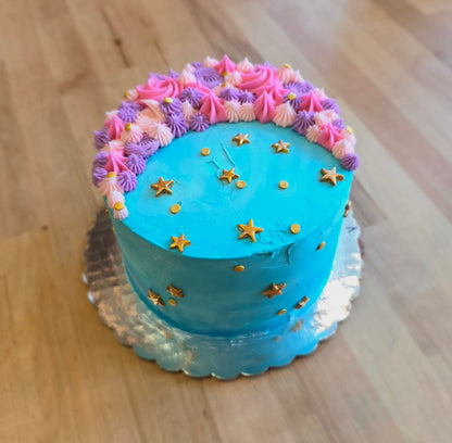 A fun moon-themed cake frosted with teal frosting, a pink and purple crescent moon, and gold stars dotting the cake; a pre-decorated cake shipped to the continental US.