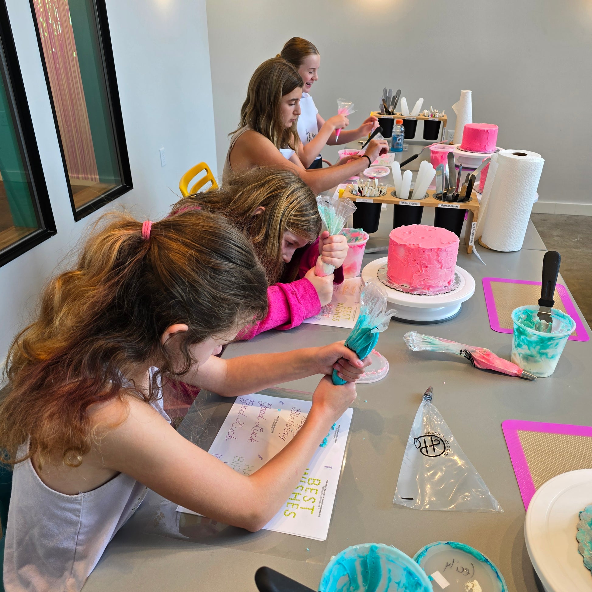 A group of kids happily decorate cakes and practice writing with frosting at a summer cake camp at Cake Hoopla in Tigard, Oregon near Portland.