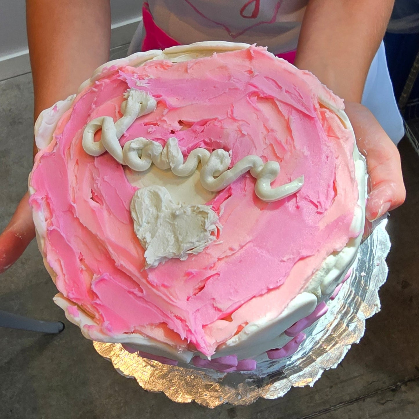 A cake decorated with Cake Hoopla's Vanilla Buttercream Frosting with the word "Lover" spelled out on top of pink-colored frosting.