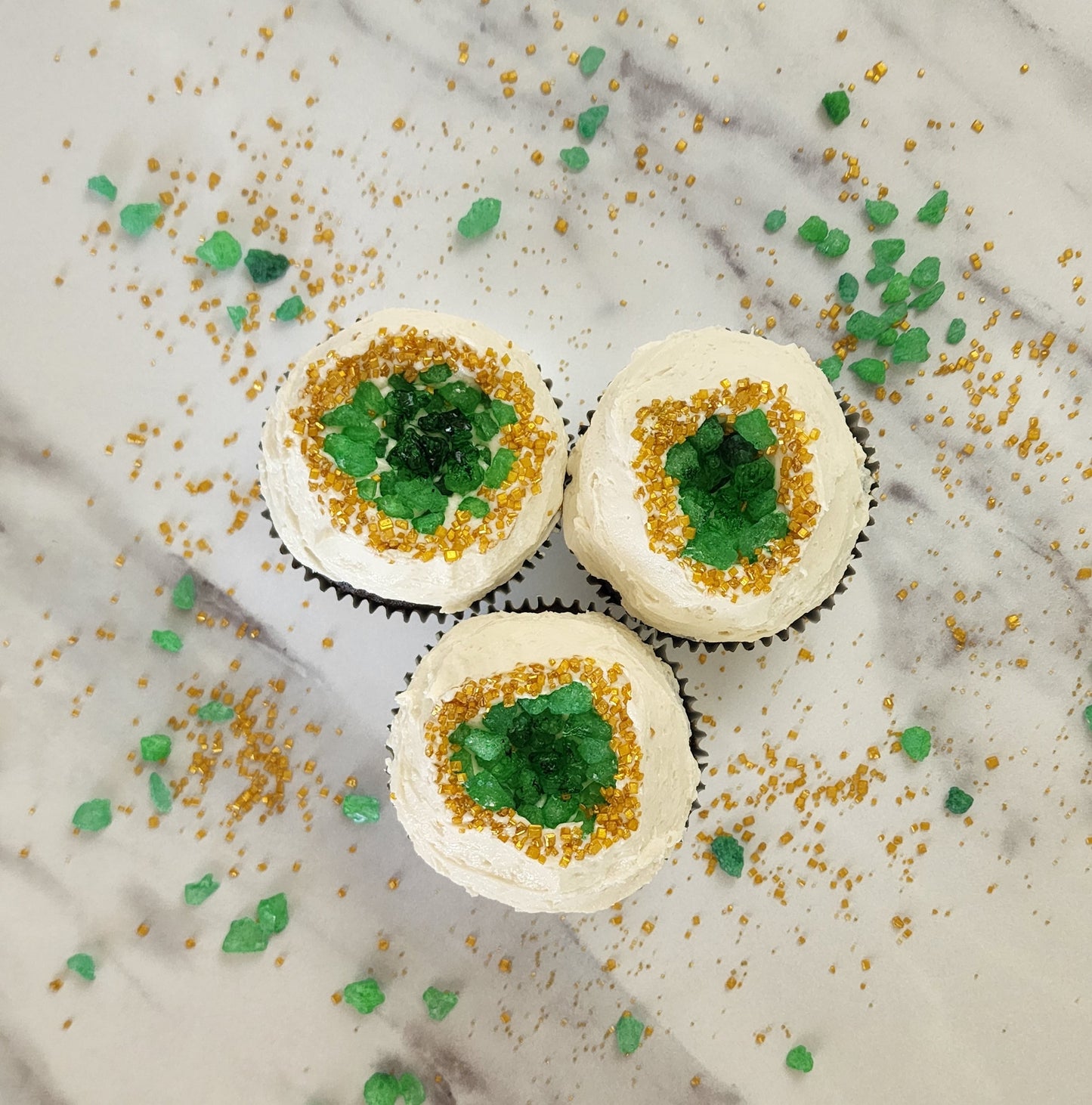 Geode cupcakes frosted white with green candy gems in the middle surrounded by gold sprinkles; a DIY cupcake kit available to decorate during open studio time at Cake Hoopla in Tigard, Oregon, in the Portland area.