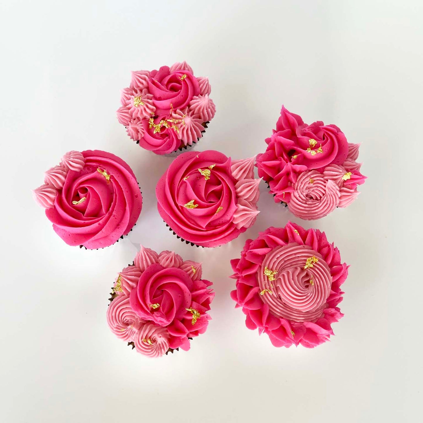 Pink floral-themed cupcakes decorated with light and dark pink rosettes and stars and gold leaf; a DIY cupcake kit available to decorate during open studio time at Cake Hoopla in Tigard, Oregon, in the Portland area.