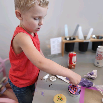 A little boy carefully adds sprinkles to his pink and purple cupcake during open studio time at Cake Hoopla in the Portland area.