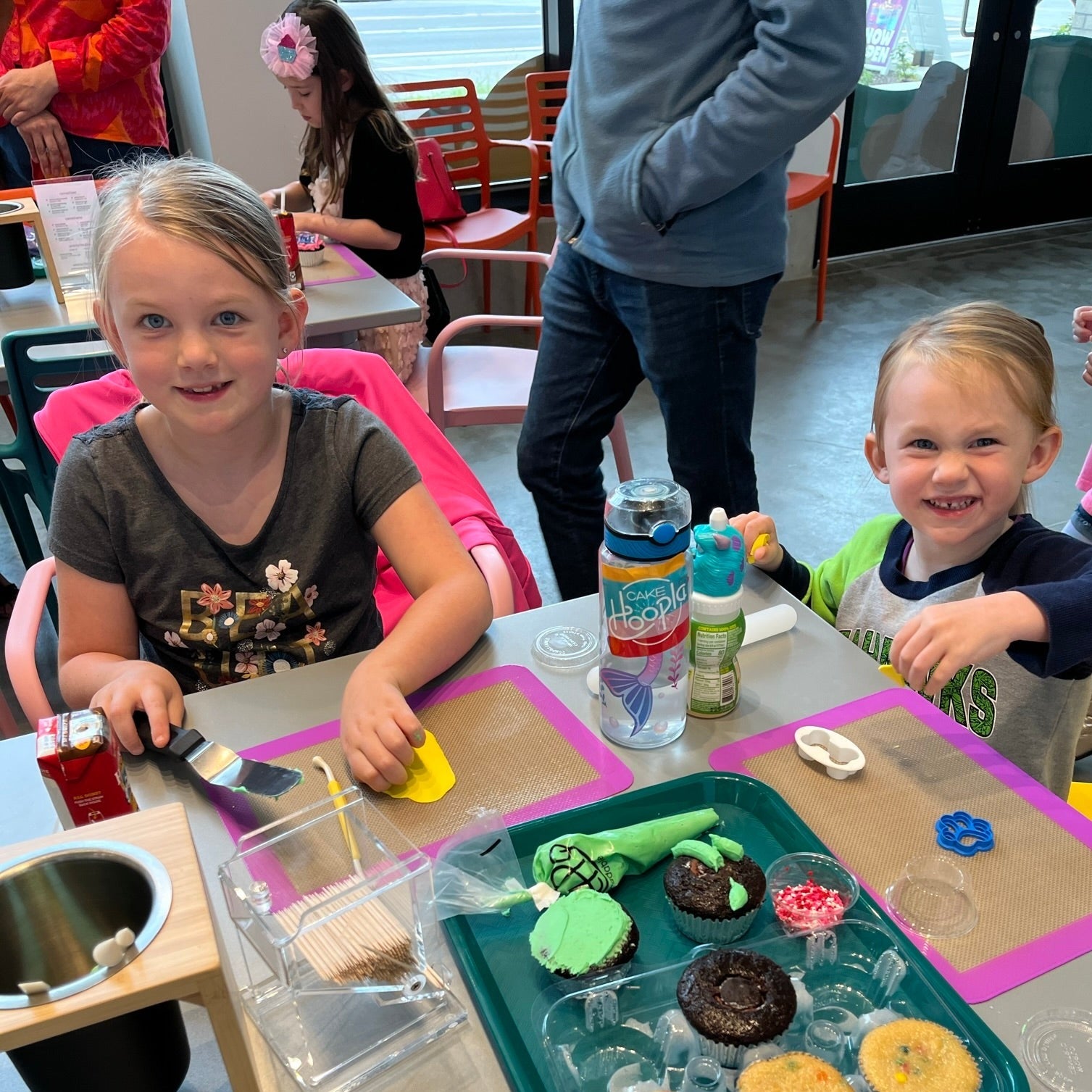 Two little girls roll out fondant to top their cupcakes from their Create Your Own Cupcake Kit during open studio time at Cake Hoopla in Tigard, Oregon near Portland.