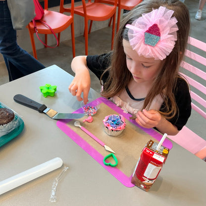 little girl adds sprinkles to her pink and purple cupcake