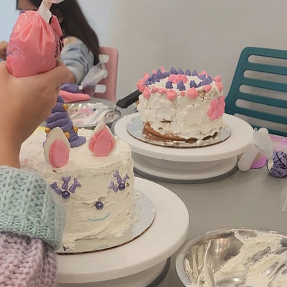 At the Cake Hoopla DIY cake/cupcake-decorating studio, kids work on their white-frosted cakes, adding white and pink ears, purple sprinkles, and a fondant unicorn horn.