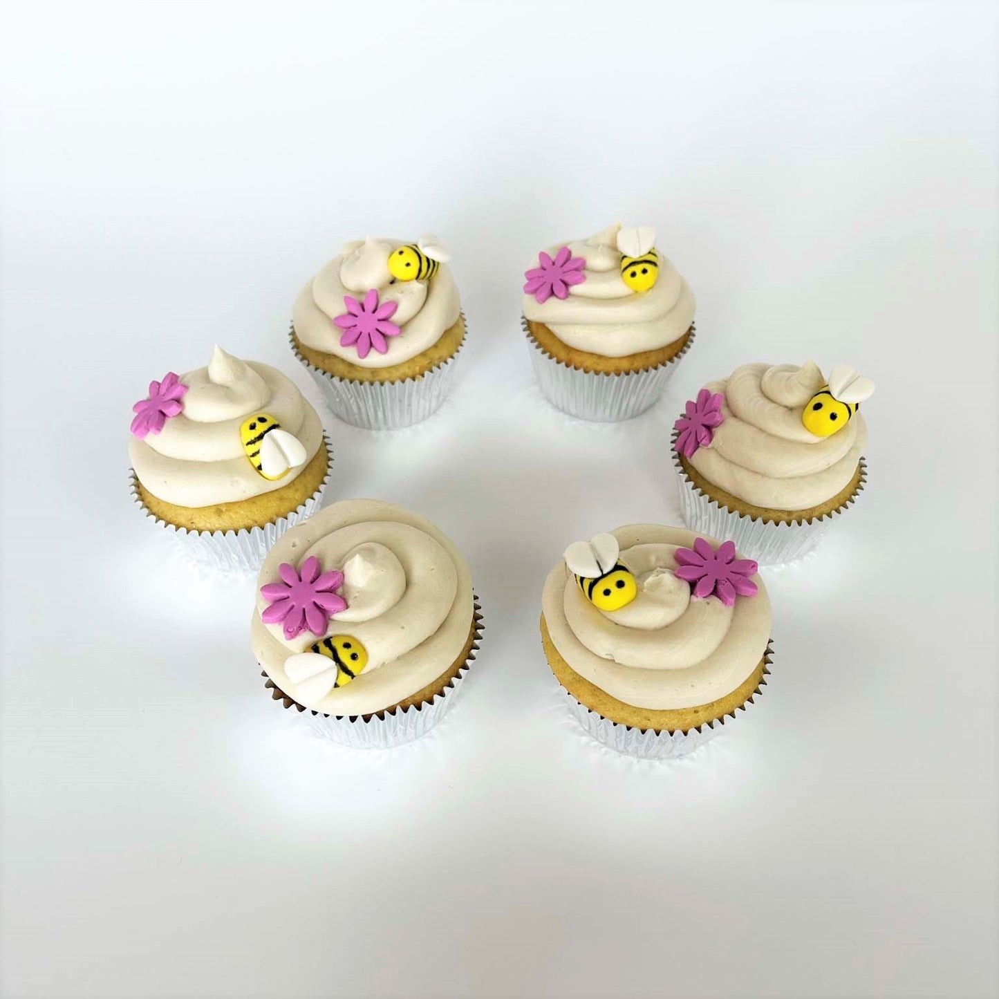 Bee-themed cupcakes frosted in white with yellow and black bumble bees and pink flowers on top; a DIY cupcake kit available to decorate during open studio time at Cake Hoopla in Tigard, Oregon, in the Portland area.