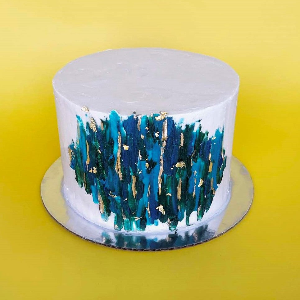 •	A white cake with teal, dark blue, and dark green streaks of frosting, like a giclee painting, and gold accents; a pre-decorated cake shipped to the continental US.