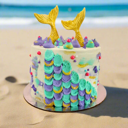 Mermaid cake with teal and purple frosting, gold mermaid tails, and pink and purple sprinkles; a pre-decorated cake shipped to the continental US.