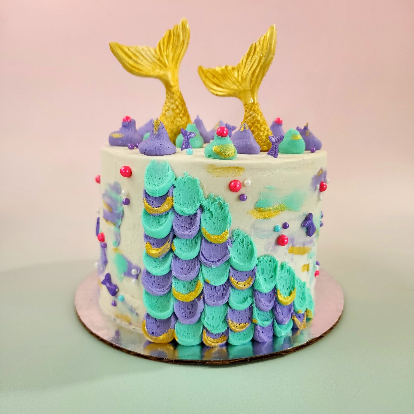 Mermaid cake with teal and purple frosting, gold mermaid tails, and pink and purple sprinkles; a DIY cake kit available to decorate during open studio time at Cake Hoopla in Tigard, Oregon, in the Portland area.