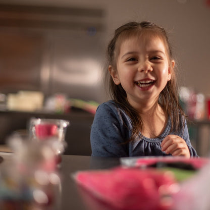 A happy girl attends a Cake Hoopla cake-decorating party with frosting, fondant, and sprinkles all around the table.