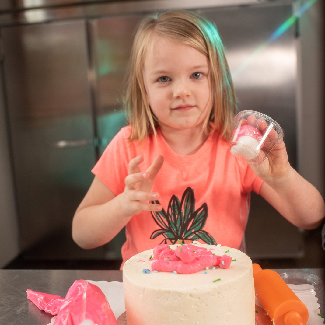 A girl decorates a Cake Hoopla cake with pink frosting and pink and white fondant.