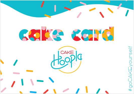 A white rectangular card reads in thick, bold lettering "cake card" in the center. The lettering is a combination of teal, pink, yellow, and red and sprinkles of the same colors cascade from the top of the card. A Cake Hoopla logo is beneath "cake card," and in a thin teal font along the right side of the card is the hashtag "goCAKEyourself."