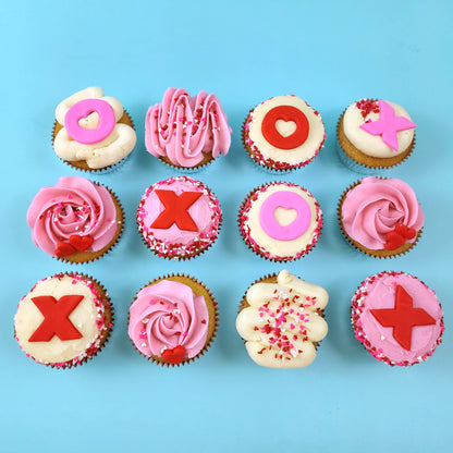 Love-themed XOXO cupcakes frosted pink and white with Xs and Os, hearts, and heart sprinkles; pre-decorated cupcakes shipped to the continental US.