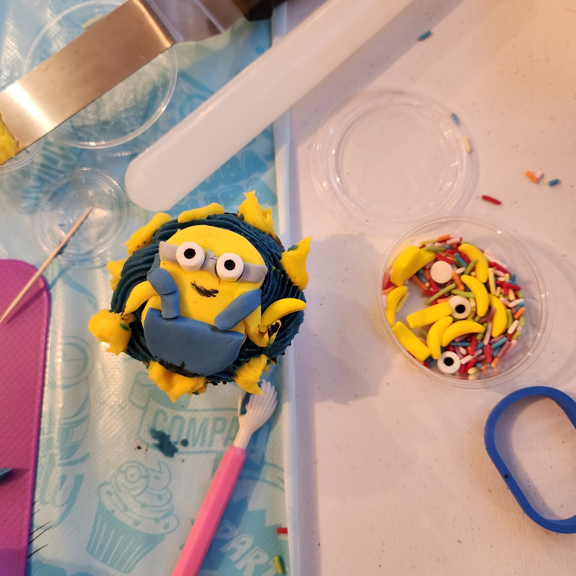 At a DIY cupcake-decorating party, a guest decorated a minion cupcake with yellow fondant, blue overalls, and banana sprinkles.