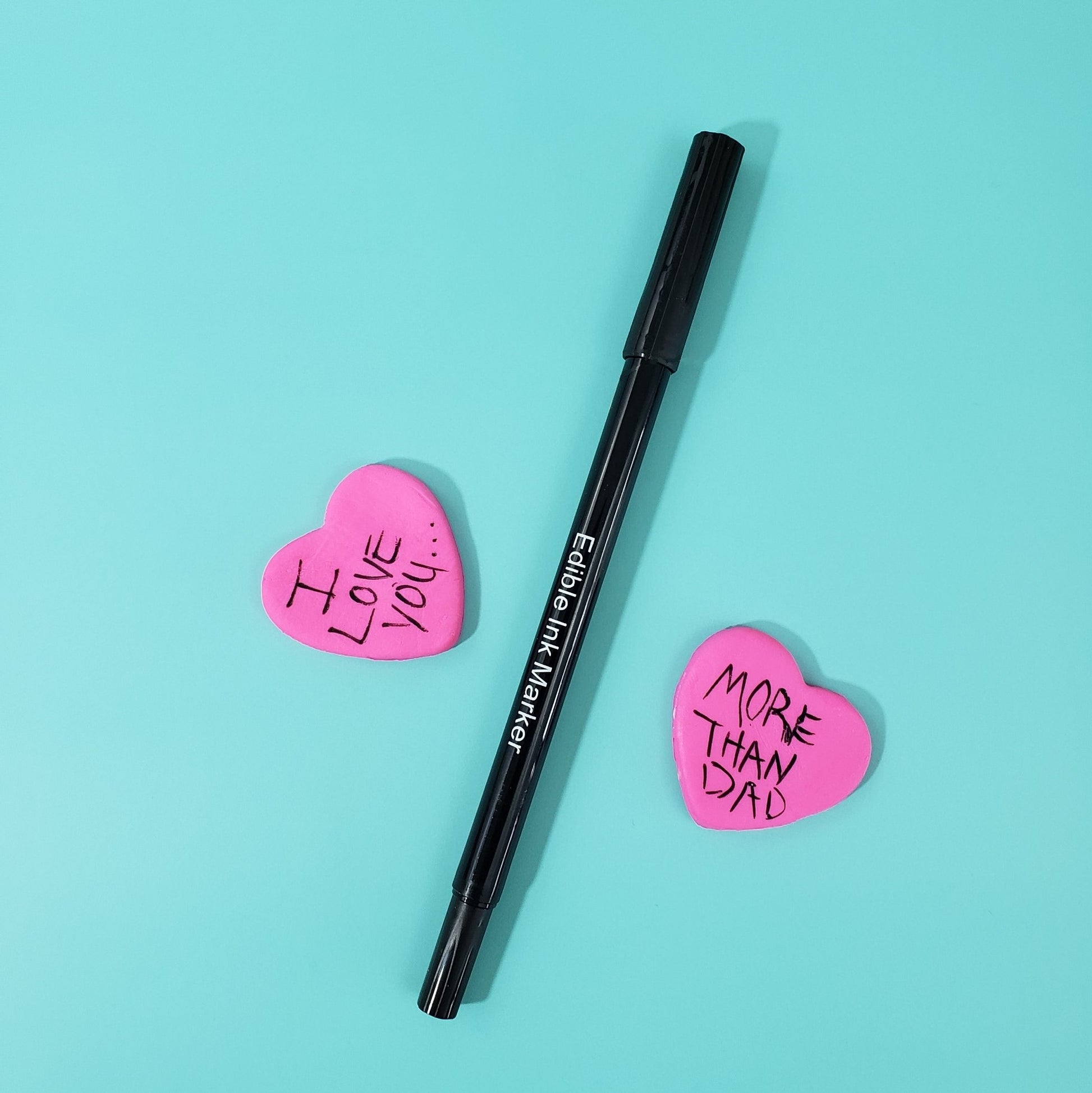 An edible black ink marker with two fondant hearts, which together read "I love you...more than dad" available withe the Mod cake kit at Cake Hoopla.